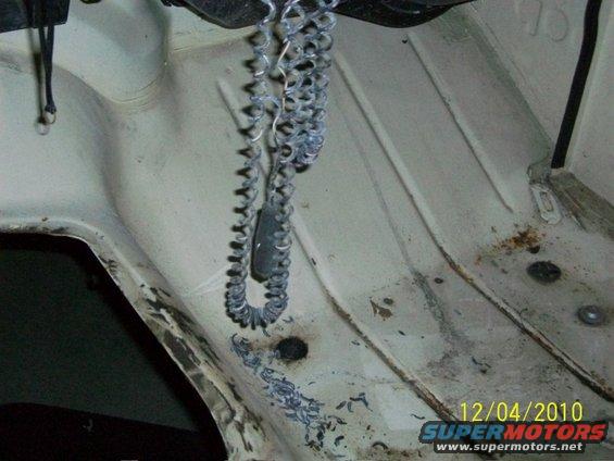 White engine bay with a coiled metal chain hanging, showing rust spots and debris