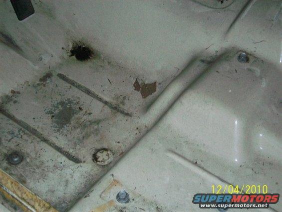 Underside of a light-colored vehicle hood with some rust and dirt