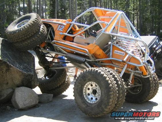 Orange off-road buggy with roll cage climbing over large rocks. Number 12 is visible on the side
