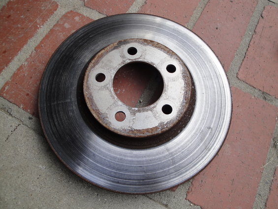 Brake rotor with five lug nut holes, resting on brick and concrete