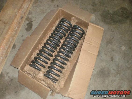Two gray coil springs packaged in a cardboard box with brown paper