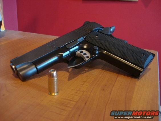 Black semi-automatic pistol with a single bullet on a wooden table