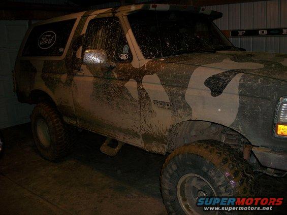 Mud-covered 1995 Ford Bronco with camouflage paint, parked indoors