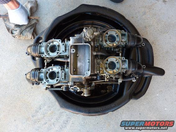 Four motorcycle carburetors disassembled and laid out in a black oil drain pan