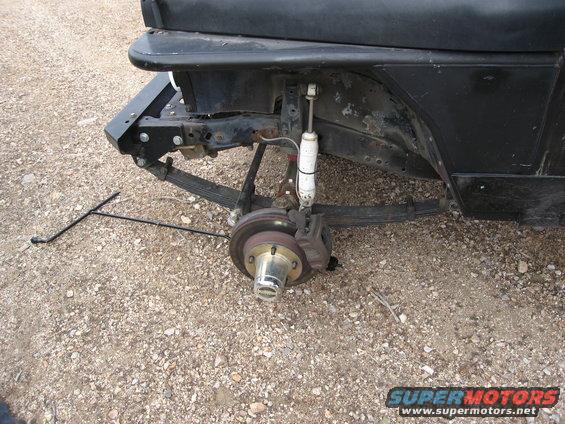 Close-up of a vehicle's rear suspension with leaf springs and shock absorber removed, showing brake rotor and hub