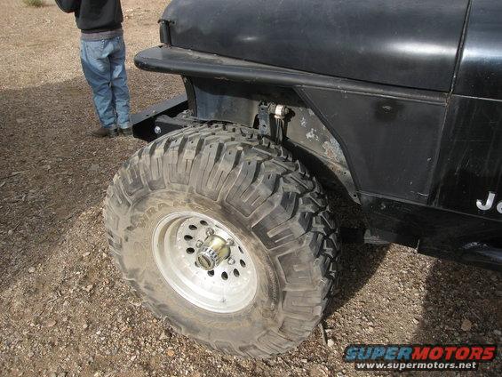 Black Jeep Wrangler front fender and large off-road tire. A person stands in the background