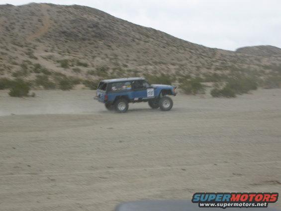 Blue SUV with lifted suspension and off-road tires driving in a desert landscape. Number 738 is visible on the door