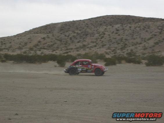 Red custom beetle-style car with racing decals driving on a dirt road