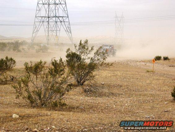Off-road vehicle driving through desert dust, with power lines overhead