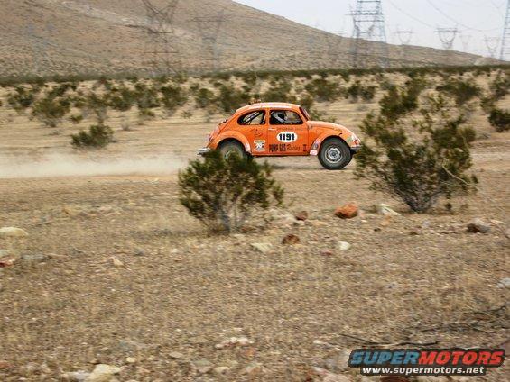 Orange Volkswagen Beetle rally car with number 1191 on door, kicking up dust