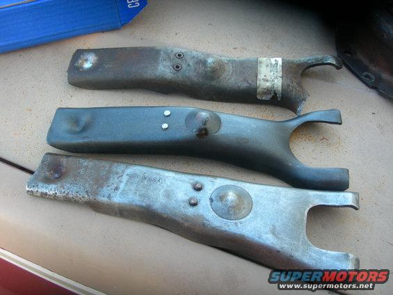Three metal clutch fork parts laid out on a surface. One has a sticker with numbers
