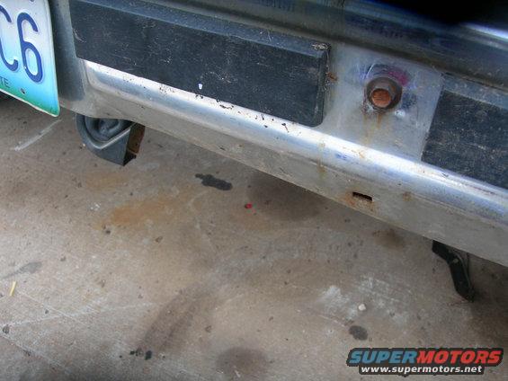 1984 Ford Bronco rear bumper with chrome trim and black rubber strip, showing a license plate and part of a tire