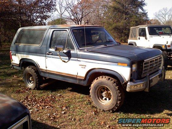 Two SUVs parked outdoors: a blue and white Ford Bronco and a white Jeep Wrangler. The Bronco is in the foreground