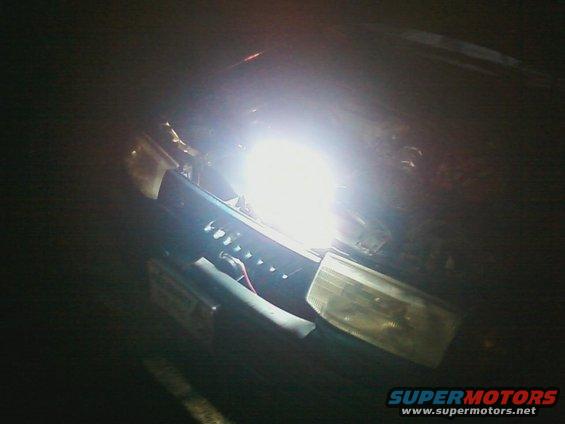 Headlight assembly with bright LED bulb, dark grille, and part of a license plate