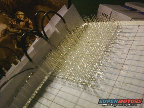 Many small LEDs with wires attached to a grid paper, bound by black rings