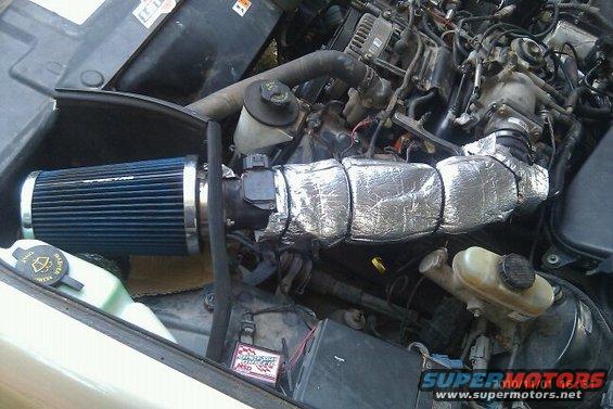 Engine bay showing a blue cone air filter connected to a silver-wrapped intake tube