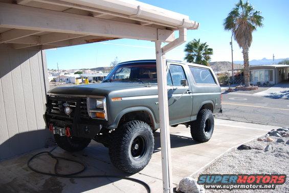 Green Ford Bronco parked under a carport, lifted with large tires