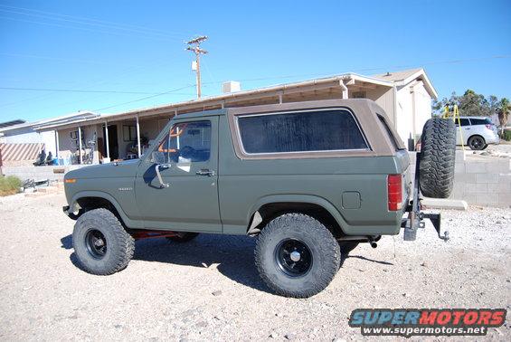 Olive green Ford Bronco with a brown soft top, lifted suspension, and a spare tire mounted on the rear