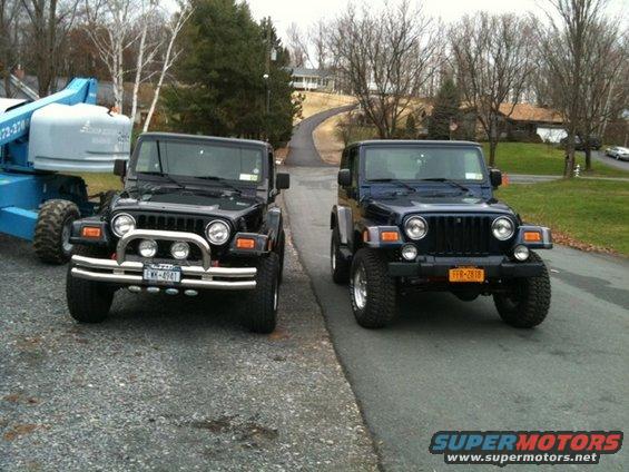 Two Jeeps parked on a road, one black and one dark blue. A blue lift is visible to the left