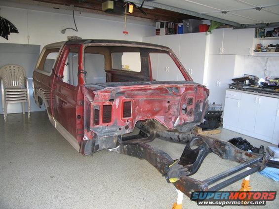 Red Ford Bronco body on jack stands, disassembled, showing frame and engine bay