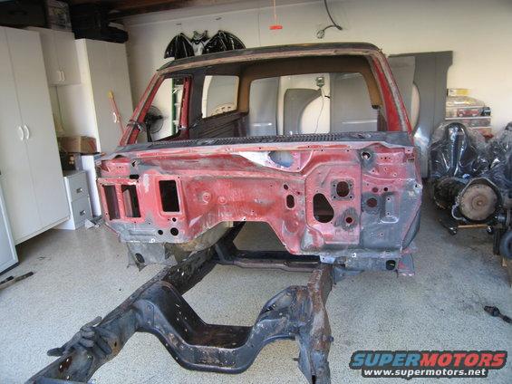 1980s Ford Bronco body shell stripped to frame, red paint, in garage