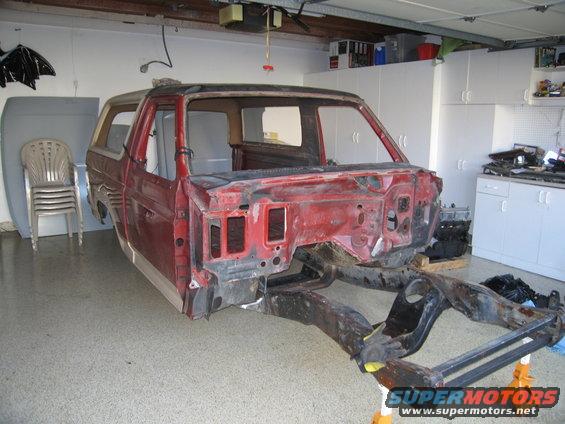 Red Ford Bronco body removed from frame, sitting in a garage