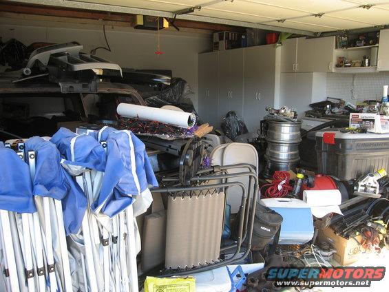 Garage interior filled with stored items, including folded tents, chairs, and car parts
