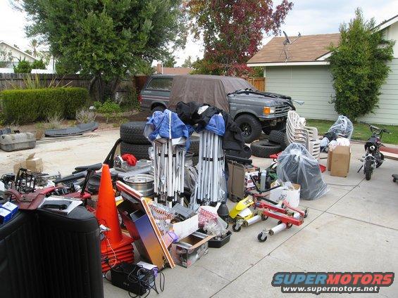 Gray Ford Bronco with a tarp covering part of it, parked in a driveway with scattered items