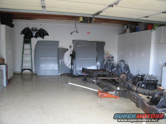 Car frame on jack stands with grey body panels leaning against wall