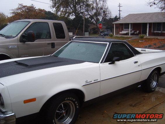 White 1973 Ford Ranchero with black hood scoop and vinyl top, parked next to a tan pickup truck