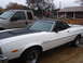 1973 Ford Ranchero - A white 1973 Ford Ranchero with a black hood scoop and vinyl top is parked next to a tan pickup truck.