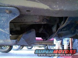 Undercarriage view of a vehicle with visible exhaust components and a person standing nearby
