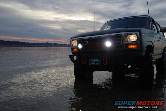 Ford Bronco with aftermarket bumper and winch parked in shallow water, dusk sky