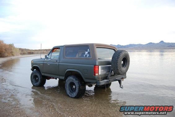 Dark green Ford Bronco with spare tire on back parked near water