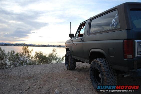 Dark green 1980s Ford Bronco with lifted suspension and off-road tires parked by a lake