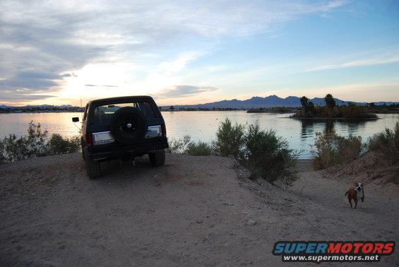 Black SUV with spare tire on rear, parked by lake at sunset