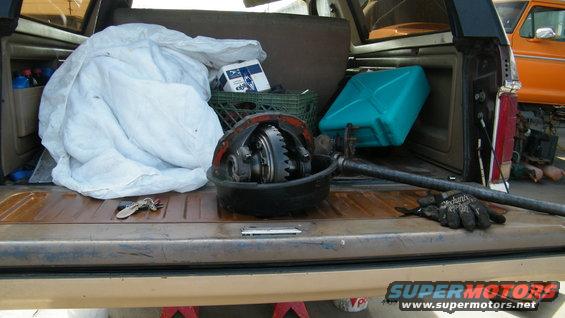 Differential assembly, white tarp, blue gas can, and milk crate in truck bed. Orange vehicle visible in background