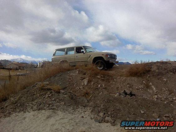 1986 Toyota Land Cruiser driving up a dirt hill with cloudy sky