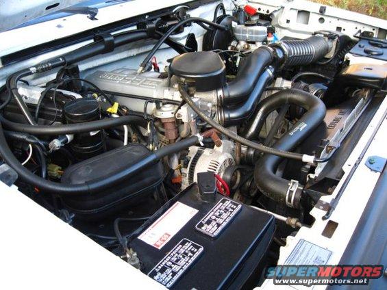 Engine bay with hoses, battery, and engine components visible