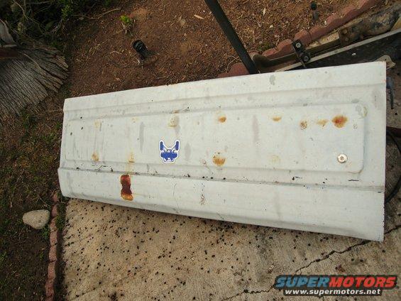 White tailgate panel with rust spots and a blue sticker of a dog's face