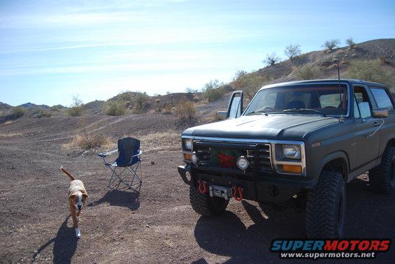 Green Ford Bronco parked in desert landscape with a dog and a chair