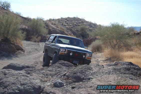 1982 Ford Bronco navigating a rough, rocky desert trail with sparse vegetation