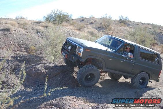 Dark green Ford Bronco climbing a rocky hill with a driver inside