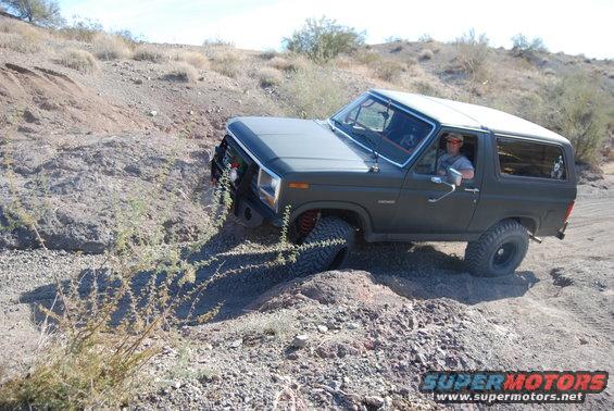 Dark gray Ford Bronco with off-road tires and bumper driving on a dirt hill