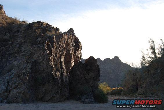 Rocky desert terrain under a bright sky, with scrub brush and distant mountains