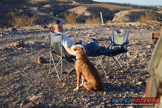 Man petting dog while sitting in camping chairs in a desert landscape
