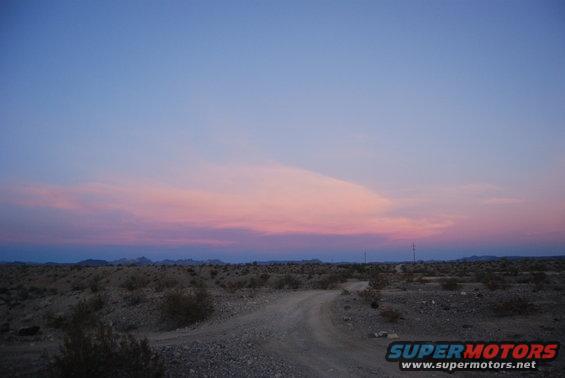 Desert landscape with dirt road under a pink and blue sky at dusk