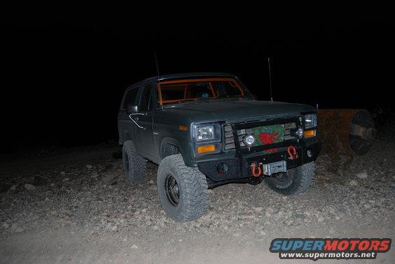 Dark green Ford Bronco with aftermarket bumper and winch, parked on gravel at night