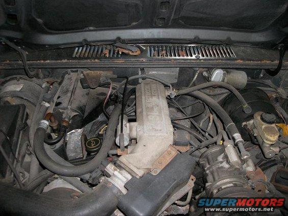 Engine bay with hoses, wires, and engine components visible. Text on engine reads 'Ford-Mazda'