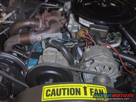 Engine bay with a turbocharger, alternator, and a yellow CAUTION FAN sticker